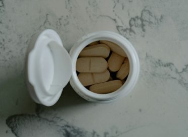 Opened bottle of beige pills on marbled surface